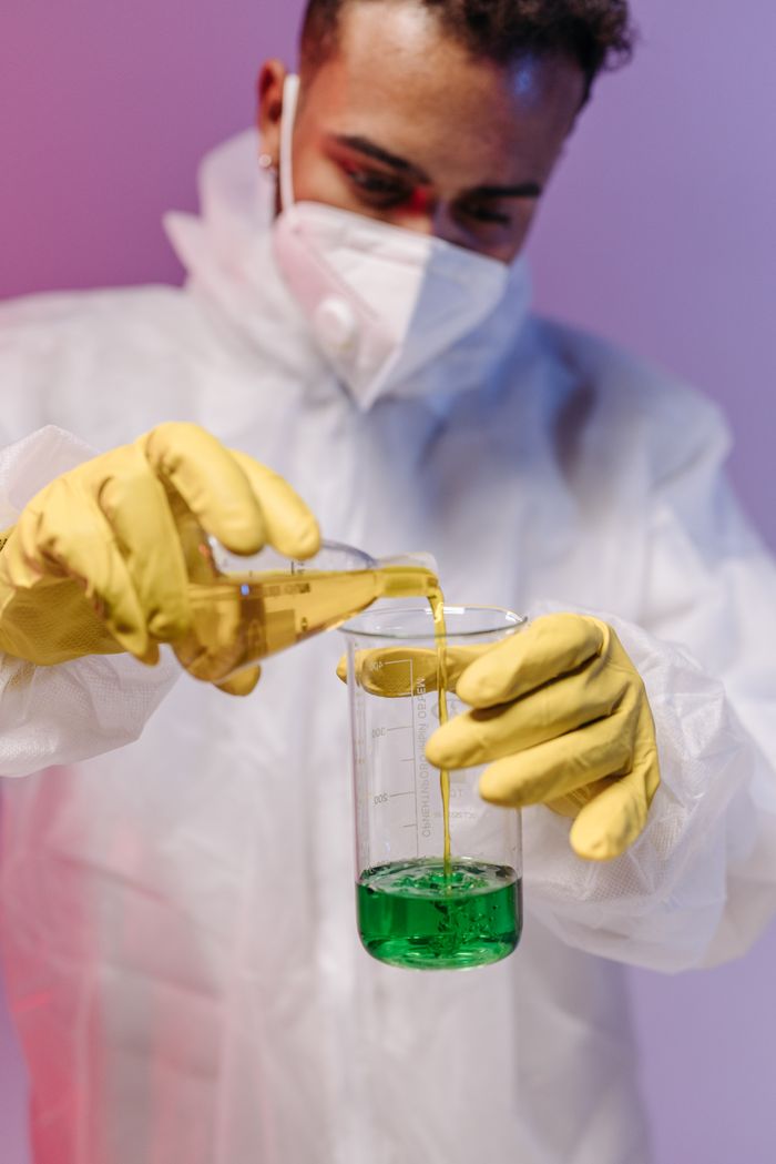 Scientist pouring chemical into beaker in laboratory setting, wearing protective gear.